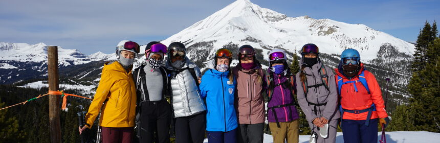 women of color stand together at the top of a ski mountain